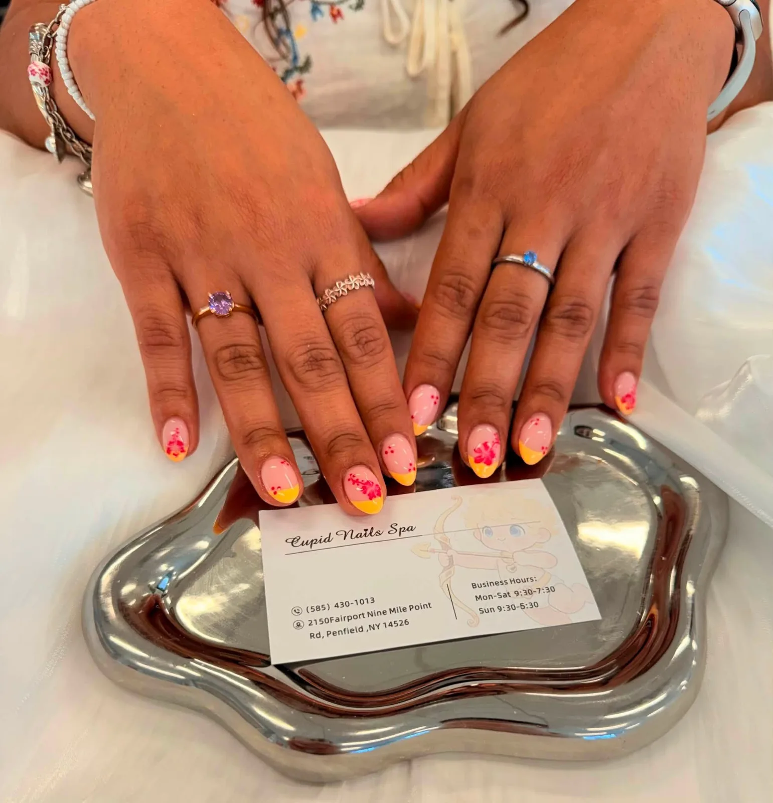 Short oval nails on a sheer pink base with bright orange tips and small red blossoms painted at the cuticle