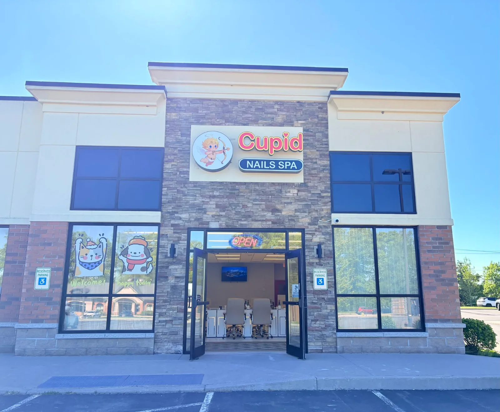 The front of Cupid Nails Spa — a stone and brick storefront with a lit sign showing a cartoon cupid drawing a bow, both glass doors propped open on a sunny day